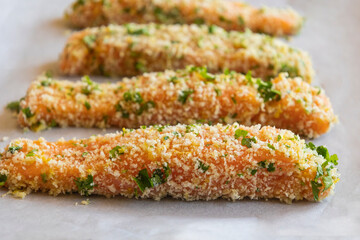 Close-up of raw breaded salmon fillets arranged in a tray, ready to be baked. The salmon is coated evenly with breadcrumbs, showing texture and freshness