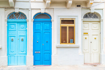Facade of a residential building with three locked wooden doors painted in light blue, blue and white color