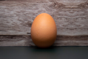 An egg standing upright leaning against a wooden coloured background while sitting on a dark green surface
