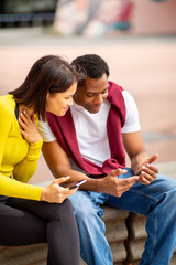 oung multicultural friends looking closely at a smartphone screen outdoors. A Black man and an...
