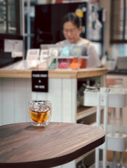 Iced coffee on table in cafe with blurred woman in background.