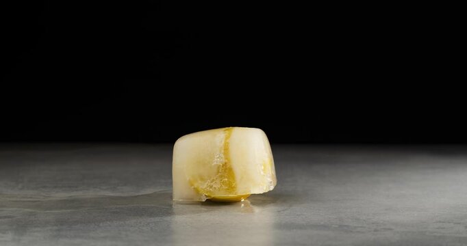 Lemon in an ice cube, close-up. Time lapse of the ice melts and a half of lemon appears. Frozen fruit. Black background.