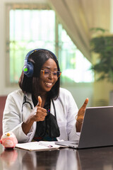 A smiling African female paedetrician wearing headphones conducts a virtual consultation on her laptop. Telehealth appointment with a patient. Convenience and accessibility of modern healthcare.