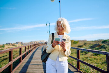 Woman checking smartphone while walking on wooden pier in sunny weather