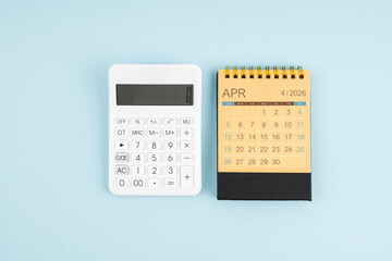 April 2026 desk calendar and calculator on blue background.