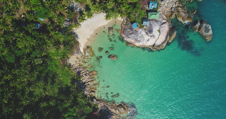 Aerial view of a tropical beach landscape with lush greenery, white sandy shore, turquoise water waves surrounded by rocks. Nature vacation concept. Thailand, Koh Phangan Island, Haad Thong Reng Beach