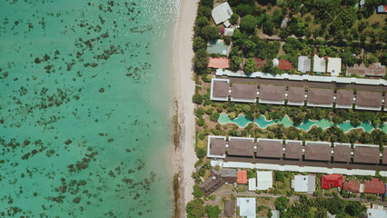 Aerial view of Tahiti island beauty, turquoise water, coral reef, sandy beach, resort hotel houses bungalows with swimming pool. Remote nature paradise, exotic summer travel. Top down drone panorama