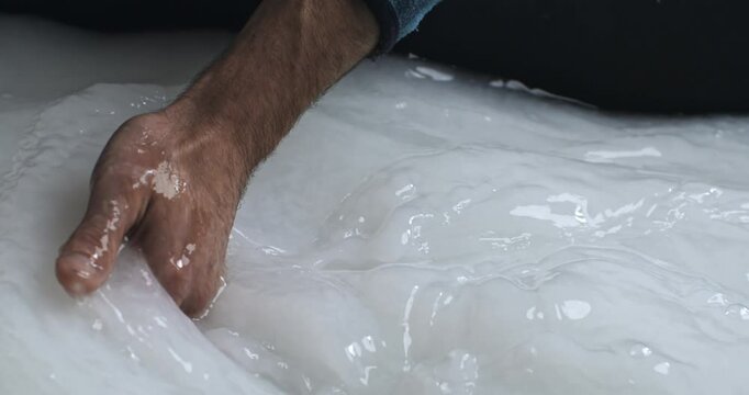 Super Slow Motion Close Up of Hand Stirring White Paper Pulp in Vat During Traditional Papermaking Process - Close-Up of Artisan Mixing Slurry for Sheet Formation in Handmade Paper Craft Workshop.