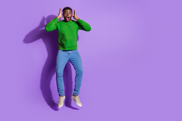 Joyful young man in casual green sweatshirt jumping with surprised expression against a vibrant...