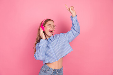 Plakat Young joyful woman in stylish attire enjoying music with headphones against a pink background expressing happiness and leisure