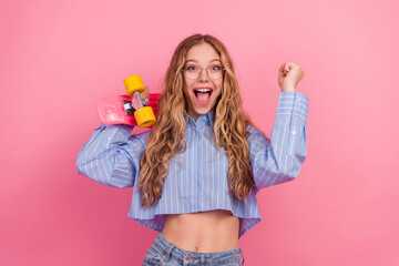 Plakat Excited young woman in striped blue shirt holding a colorful skateboard, enjoying leisure time on a pink background
