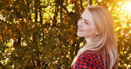 Nature, happy and woman by trees with sunshine for wellness, fresh air and relax outdoors. Countryside, smile and person in forest, woods and morning for calm, joy and freedom in natural environment