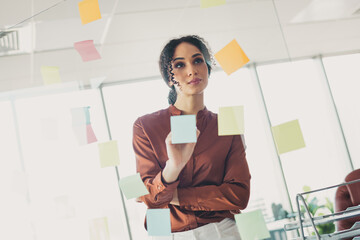 Young businesswoman brainstorming ideas in a modern office while organizing colorful sticky notes...