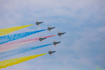 Six fighter jets fly in formation leaving colorful smoke trails across a clear blue sky.
