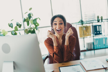 Young businesswoman celebrating success at her office desk surrounded by plants and natural...