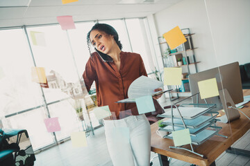 Confident businesswoman multitasking on the phone while organizing her work in a bright and modern...
