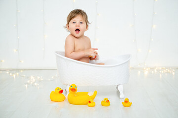 A baby boy is bathing in a bubble bath and playing with rubber ducklings for bathing on a white...