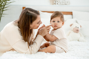mom and baby on the bed at home hugging and kissing, mother and child playing and having fun, happy motherhood and a young family