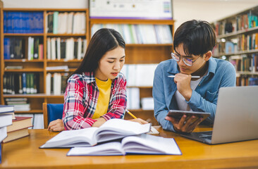 Students are consulting each other working on laptops and searching for books to study, make reports, find useful information in university room. Concept of reading, learning and intelligence.