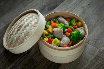 温野菜が入った天然竹製のせいろと木目フローリング背景