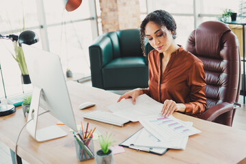 Professional businesswoman analyzing reports at her desk in a modern office with natural lighting...