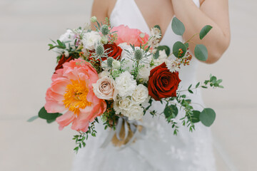 Bride holds a vibrant bouquet of flowers while wearing a white wedding dress outdoors in a joyful...
