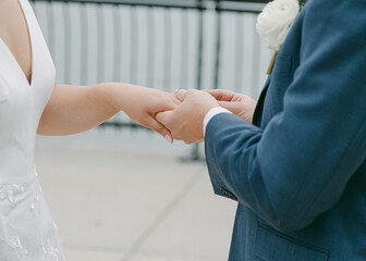 Fototapeta premium Couple exchanges wedding rings at waterfront venue during outdoor ceremony on a sunny afternoon