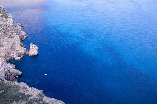 Solitary Boat Floating in Clear Blue Mediterranean Sea Near Rocky Cliffs