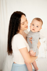 mom and baby, mother hugs and kisses baby holding him in her arms, maternal love and care, young mom having fun with baby baby, mom's decree