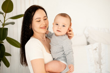 mom and baby, mother hugs and kisses baby holding him in her arms, maternal love and care, young mom having fun with baby baby, mom's decree