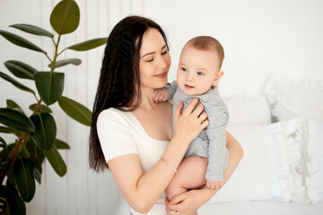 mom and baby, mother hugs and kisses baby holding him in her arms, maternal love and care, young mom having fun with baby baby, mom's decree