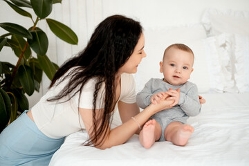 mom and baby, mother hugs and kisses baby holding him in her arms, maternal love and care, young mom having fun with baby baby, mom's decree