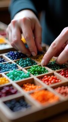 Organized hands sorting colorful beads in wooden box.