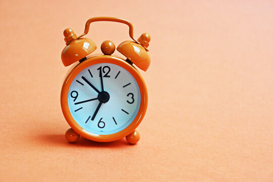 Small vintage orange alarm clock on an orange background 