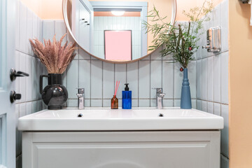 a large white sink in the bathroom, a round mirror, blue tiles on the walls, vases with flowers,...