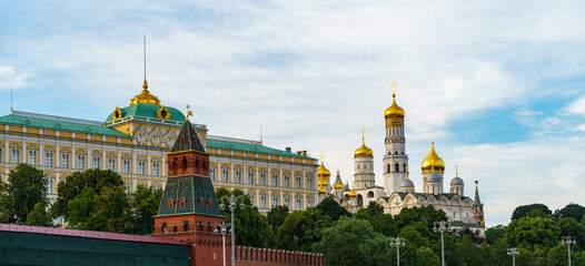 Picturesque view of Moscow's Kremlin towers rising above lush green trees, with historic architecture under clear blue sky