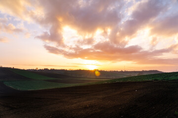 typical sunrise in the Polish countryside, spring, beautiful greenery, black soil, crops, clouds and flare as a physical phenomenon