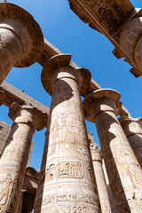 A low angle view showcases the monumental columns of Karnak Temple, Egypt, reaching towards a clear...