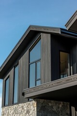 Modern architectural design of a dark wood and stone house under clear blue sky during daytime with expansive windows showcasing a contemporary style