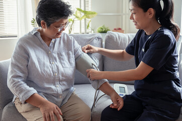 Young Asian woman nurse take care senior woman at nursing home, checking blood pressure for observe...