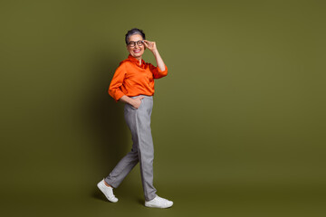 Confident mature woman in stylish attire walking against green backdrop exuding charm and elegance with a bright smile