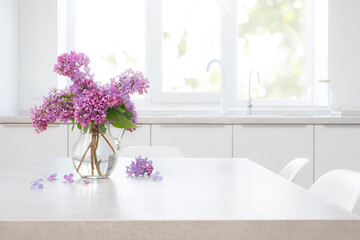 Lilac flowers and twigs with glass vase on table in light colors kitchen interior background