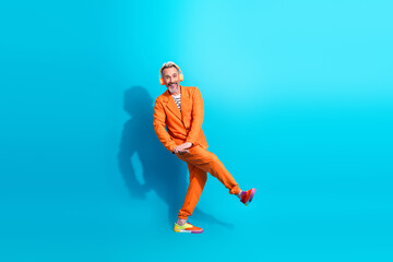 Trendy middle aged man in an orange suit happily poses with a vibrant blue background showcasing vibrant and colorful fashion concepts.