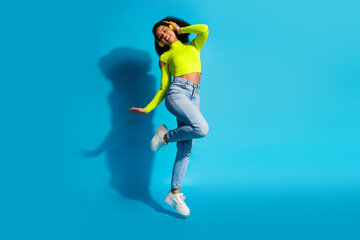 Obraz premium Young vibrant woman in neon outfit joyfully posing against a blue studio background, highlighting casual fashion and cheerful lifestyle