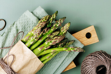 Asparagus bundle in paper wrap placed on wooden board and green towel