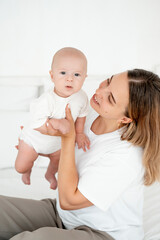 a young beautiful mother with a baby boy hugging on the bed at home in the bedroom, mother's care...
