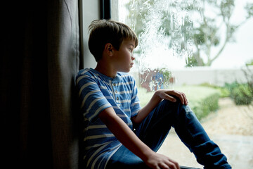 Sad, boy kid and thinking by window with depression, abandoned or unhappy for loneliness. Person,...