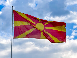 A vivid flag of Macedonia flutters proudly on a pole, showcasing its bright red and yellow colors under a partly cloudy sky during the day