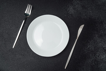 Table setting with utensils and an empty plate on a dark surface