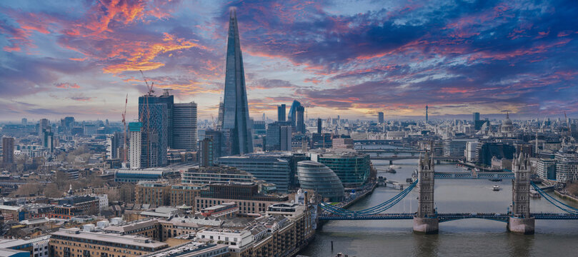 Aerial perspective of London featuring Tower Bridge over the River Thames, The Shard, City Hall, St. Paul's Cathedral, and the BT Tower under a clear sky.